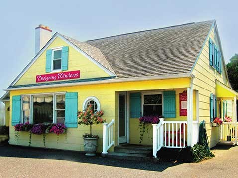 Exterior shot of a yellow house with blue shutters decorated with red flowers